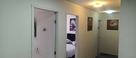 Pasillo de hotel con puertas numeradas 31 y 32, una cama con colcha estampada floral y obras de arte en las paredes.
