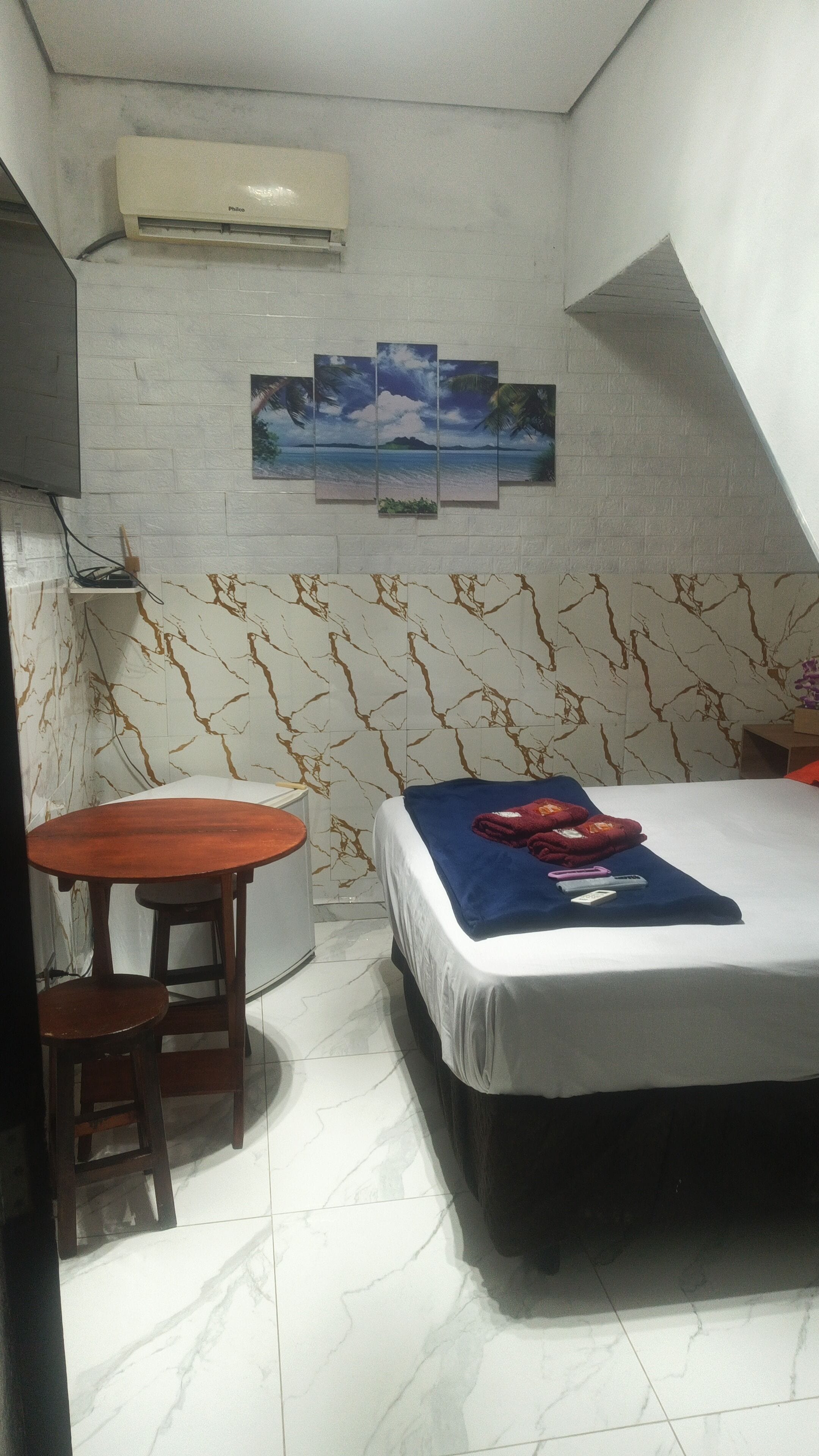 Una habitación pequeña y funcional con cama, mesa y aire acondicionado instalado en la pared.