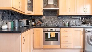 Une cuisine moderne avec des meubles en bois, un four en acier inoxydable, un four à micro-ondes et un lave-linge.