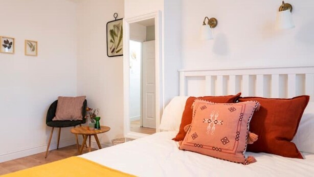 Une chambre à coucher comprenant un lit, une chaise, une petite table et une porte donnant sur une autre pièce.