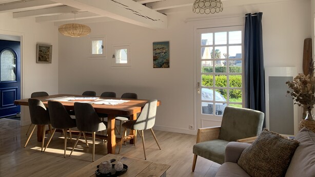 Een eetgedeelte met een houten tafel en stoelen, een bijzettafeltje met decoratieve items, en een uitzicht door een groot raam.