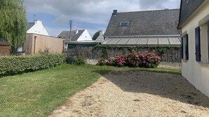 Een woonwijk met een grindpad, een tuin met roze bloemen, en huizen met uiteenlopende dakstijlen.
