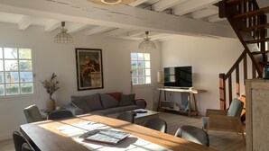 Een ruime woonkamer met een houten eettafel, zithoek, televisie en een trap.