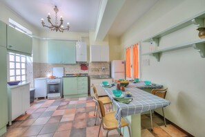 Una cucina con zona pranzo, caratterizzata da un pavimento piastrellato, un fornello, un frigorifero e un lampadario.