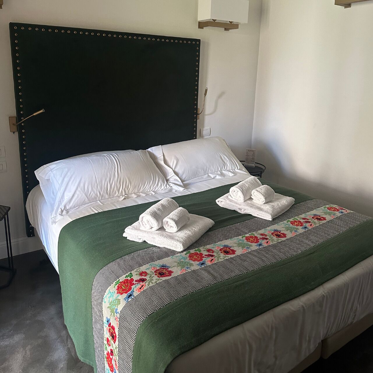 Un lit bien fait, avec des draps blancs, une couvre-lit verte à motifs floraux et deux serviettes pliées posées sur le lit.