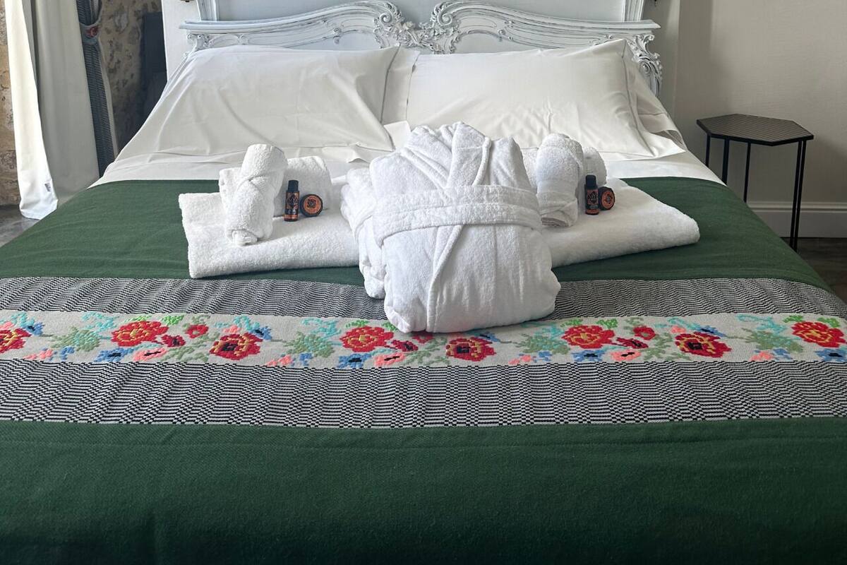A bed with white linens, a green bedspread, and a floral-patterned runner.