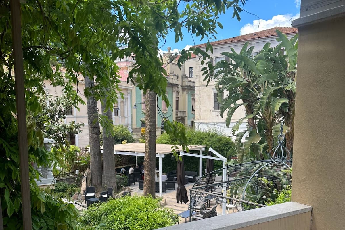 A balcony with a view of a courtyard, featuring outdoor seating and a pergola.