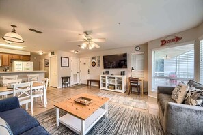 Amplia sala de estar con mesa de comedor, sofás, una mesa de centro y televisor. Hay una zona de cocina con armarios y refrigerador.