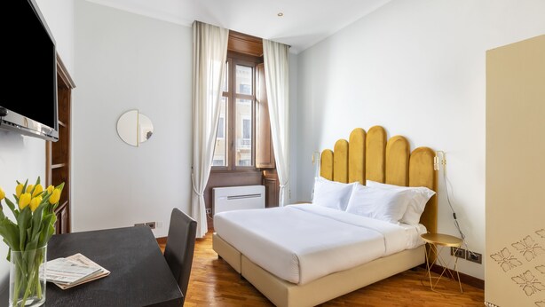 Ein Hotelzimmer mit Bett, Schreibtisch, Fernseher und einem Fenster mit Vorhängen.
