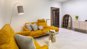 Ein modernes Wohnzimmer mit einem senffarbenen Sofa, einer Stehlampe und einem kleinen Beistelltisch.