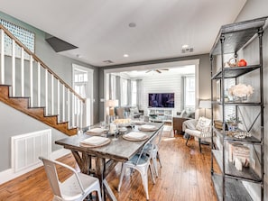 A spacious living room with a wooden dining table, comfortable seating, and a bookshelf.