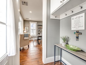 A hallway with a dining area, a sofa, a console table with a plant, and a motivational quote on the wall.