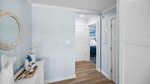 Un pasillo con paredes azul claro, suelo de madera, una puerta blanca y un espejo con marco decorativo.