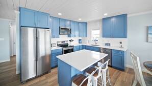 Una cocina moderna con armarios azules, un refrigerador de acero inoxidable, un microondas y una isla grande con taburetes de bar.
