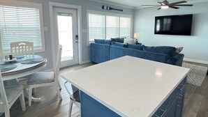 Una cocina moderna con una isla central, un área de comedor con mesa y sillas, un sofá azul y un ventilador de techo.