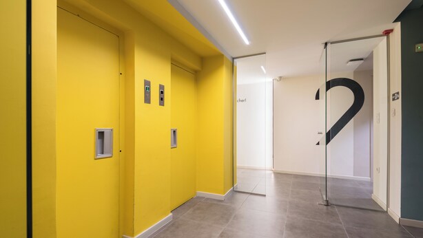Un pasillo con paredes amarillas, una puerta de vidrio con el número 2 grande en negro y un accesorio de iluminación en el techo.