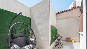 Una silla colgante con cojines, una mesita con sillas y plantas en macetas en un patio.