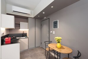 A compact kitchen with modern appliances, a dining area with a wooden table and chairs, and a grey wall with a framed picture. - M17 Studios & Suites (Athens)
