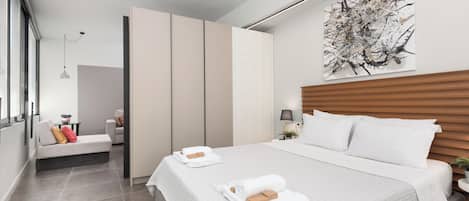 A modern hotel room with a large bed, a seating area, and a view of the city.