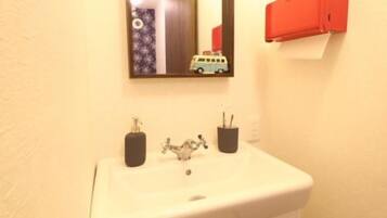 Une salle de bain avec un lavabo blanc, un miroir, un meuble rouge et le reflet d’une voiture jouet.