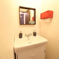 Un baño con un lavamanos blanco, un espejo, un armario rojo y el reflejo de un coche de juguete.