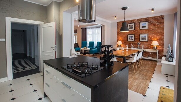 Une cuisine moderne avec un îlot central, un coin repas avec un mur en briques et un salon avec des fauteuils bleus.
