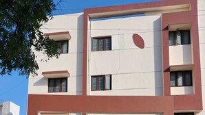 Un edificio residencial de varios pisos con techo plano, un coche estacionado en la entrada y cielo despejado.