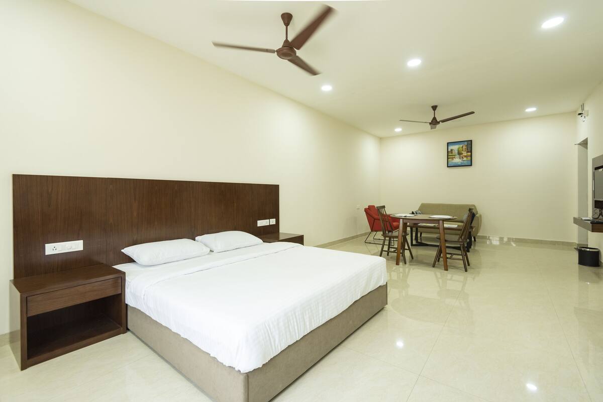 Une chambre d’hôtel avec un grand lit, deux tables de chevet, un bureau avec des chaises et deux ventilateurs de plafond.