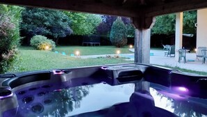 A hot tub area with a wooden ceiling and a view of a garden with trees and a lawn.