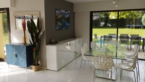 A modern dining area with a glass table and white chairs, a white counter with a blue patterned cabinet, and a painting on the wall.