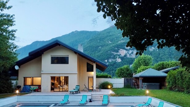 A modern house with a swimming pool, a covered patio, and a mountain backdrop.
