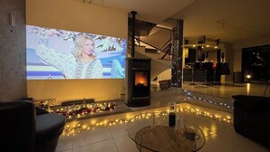 A modern living room with a fireplace, a large TV screen, and a cozy seating area with string lights.