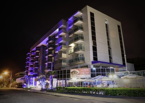 Un hotel moderno con varios balcones, una zona de estar exterior cubierta y una entrada bien iluminada.