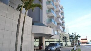 A modern hotel with a curved entrance, multiple balconies, and palm trees. - Flat pé na areia com vista internet e ar (Macaé)