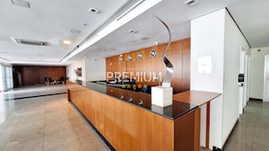 A modern reception desk with a wooden finish, a metal sculpture, and a series of clocks on the wall. - Flat pé na areia com vista internet e ar (Macaé)