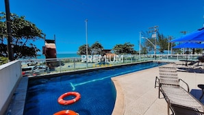 A swimming pool with a clear view of the sea, lounge chairs, and umbrellas. - Flat pé na areia com vista internet e ar (Macaé)