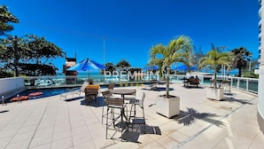 A rooftop pool area with lounge chairs, umbrellas, and a view of the sea. - Flat pé na areia com vista internet e ar (Macaé)