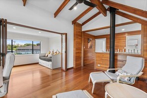 Relax in a spacious room with a high ceiling and exposed beams, featuring a seating area and a balcony with a view of the surrounding landscape.