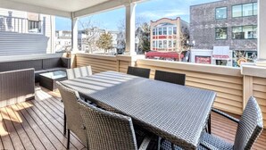 En täckt uteplats med ett matbord och stolar, en soffa och utsikt över stadsbilden.