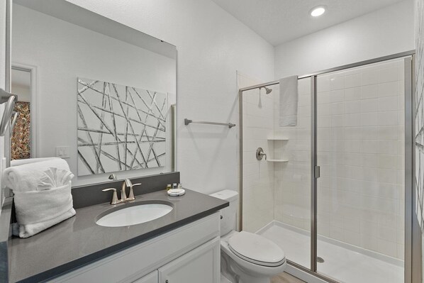 A modern bathroom with a large mirror, a sink, a toilet, and a glass-enclosed shower.