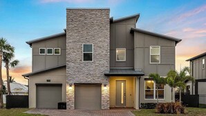 A modern two-story house with a stone facade, two garages, and a well-maintained lawn.