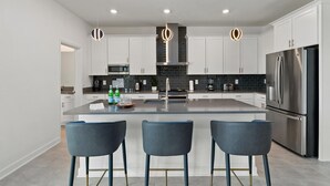 A modern kitchen with white cabinets, a stainless steel refrigerator, and a central island with bar stools.