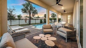 A covered outdoor patio with lounge chairs, a pool, and a table area.