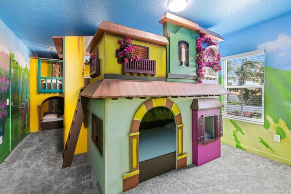 A colorful playhouse with a balcony, arched doorways, and a window.