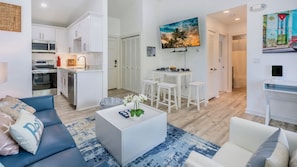 A modern apartment with a living room, kitchen, dining area, and a small office space.