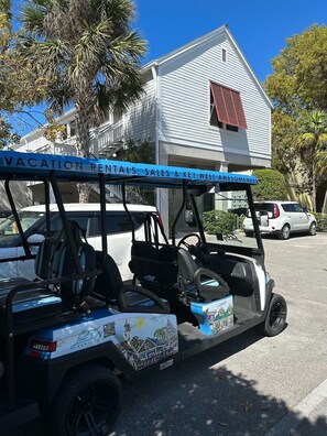 A row of golf carts parked in a parking lot with a building labeled "VACATION RENTALS, SALES & KEY WEST AWESOMENESS" in the background.