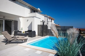Et moderne hus med swimmingpool, udendørs møbler og havudsigt.