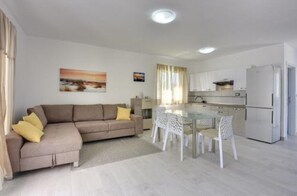 A modern living room with a sofa and a dining table with chairs. There is a kitchen area with cabinets and a refrigerator. - Villa Residence Oli B (Ližnjan)