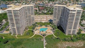 A high-rise hotel with a central courtyard featuring a swimming pool, surrounded by lush greenery and a beach. - Beachfront I Full Coastal Contemporary Renovation (Marco Island)