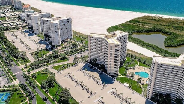A high-rise hotel with a pool, beachfront view, and a parking lot. - Beachfront I Full Coastal Contemporary Renovation (Marco Island)